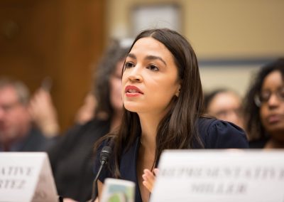 Representative Ocasio-Cortez speaking on a panel before the House of Representatives Committee on Oversight and Reform. She is speaking and looking up.