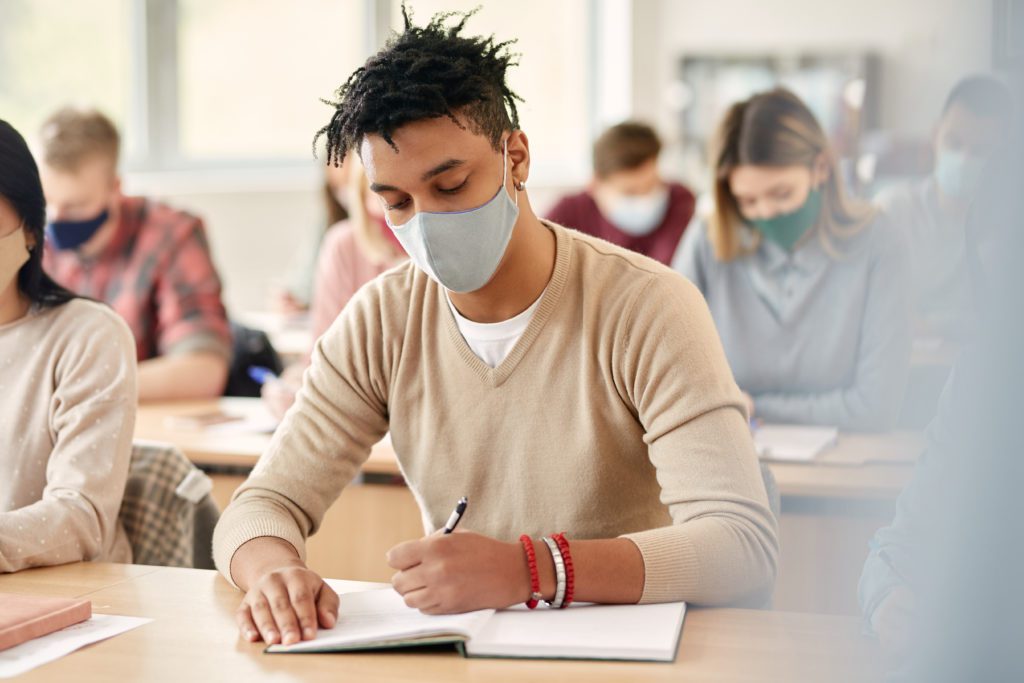 Student with mask on taking notes in a classroom.